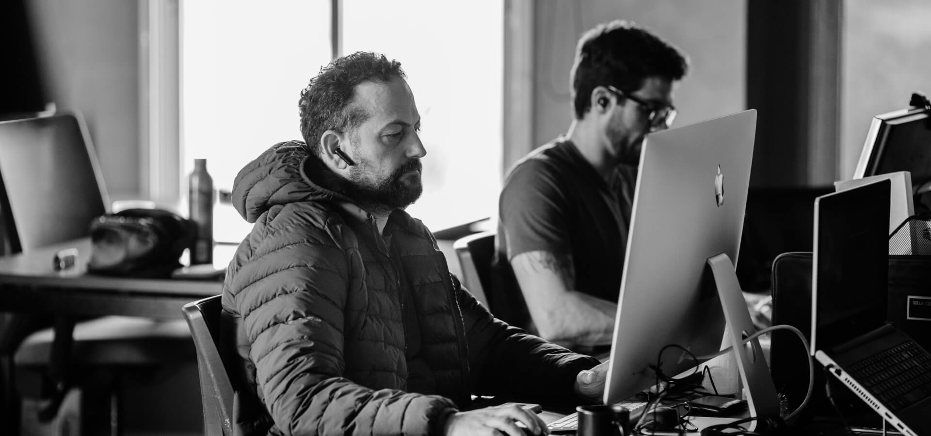 Two developers focused on work at their desks with multiple monitors and devices