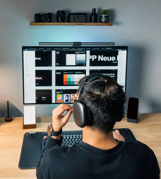 Person with headphones working at a desk with a large monitor