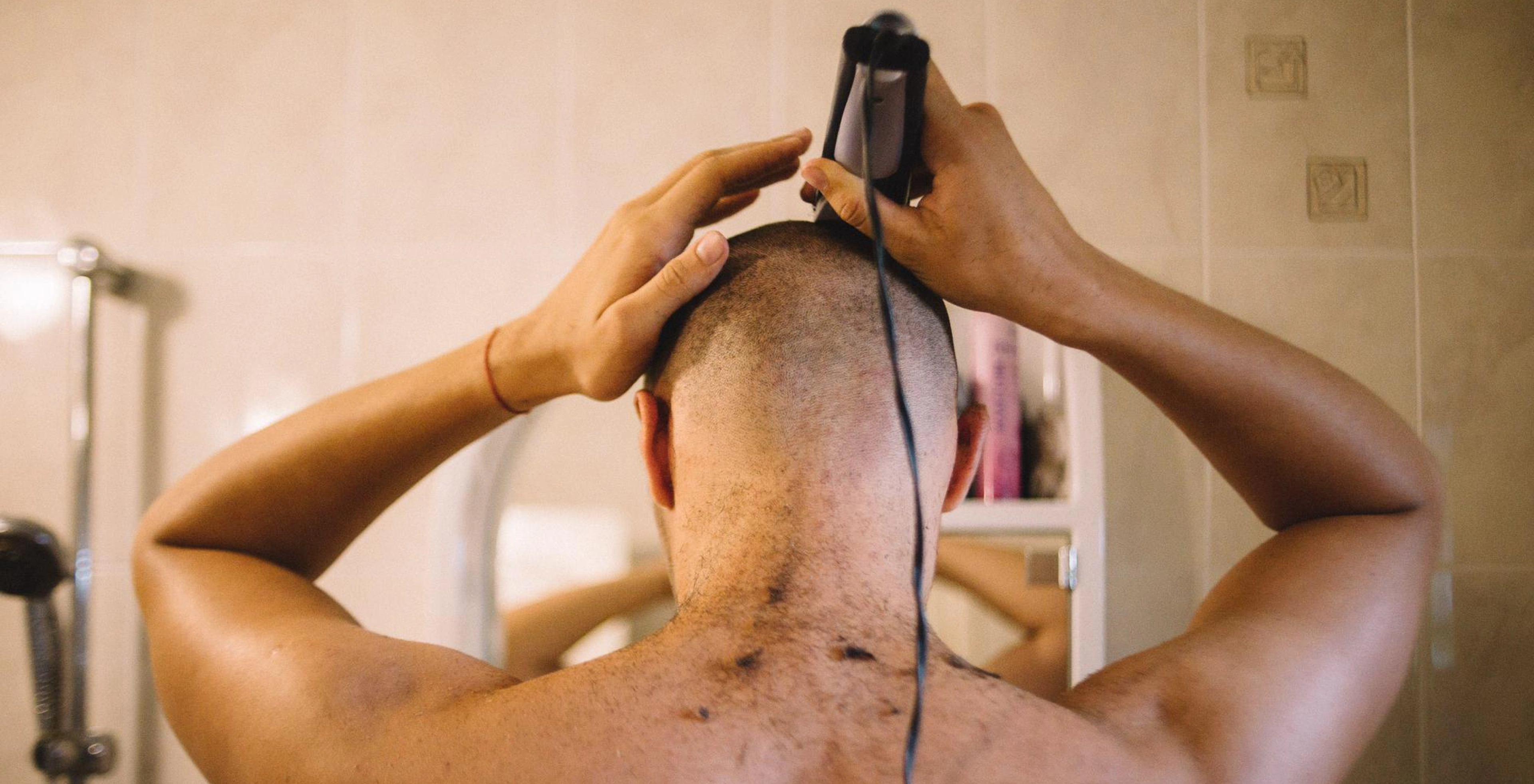 Man shaving head in mirror with clipper